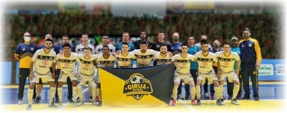 Foto posada do primeiro elenco da história do Giruá Futsal, reunindo jogadores e comissão técnica na quadra, segurando a bandeira com o escudo do time à frente.